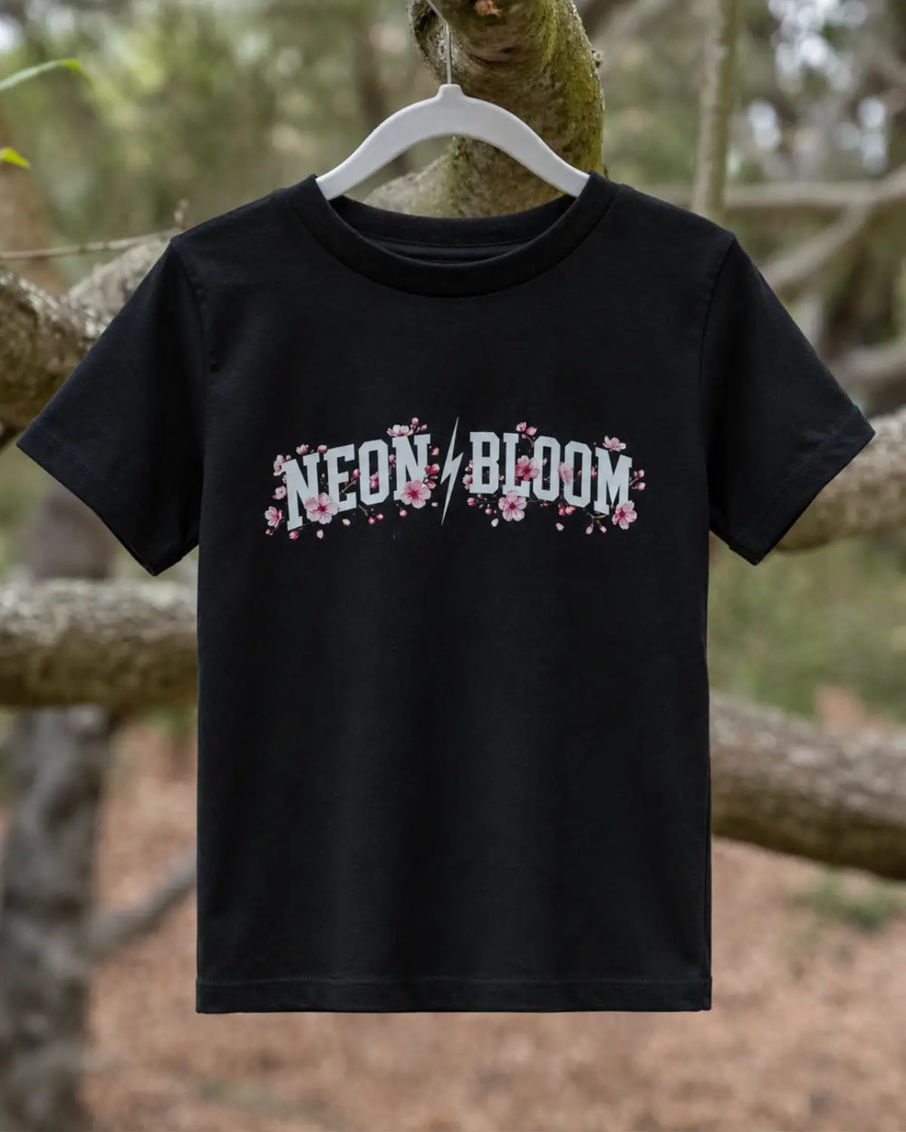 Black t-shirt with 'NEON BLOOM' text with cherry blossoms on a hanger against a natural background