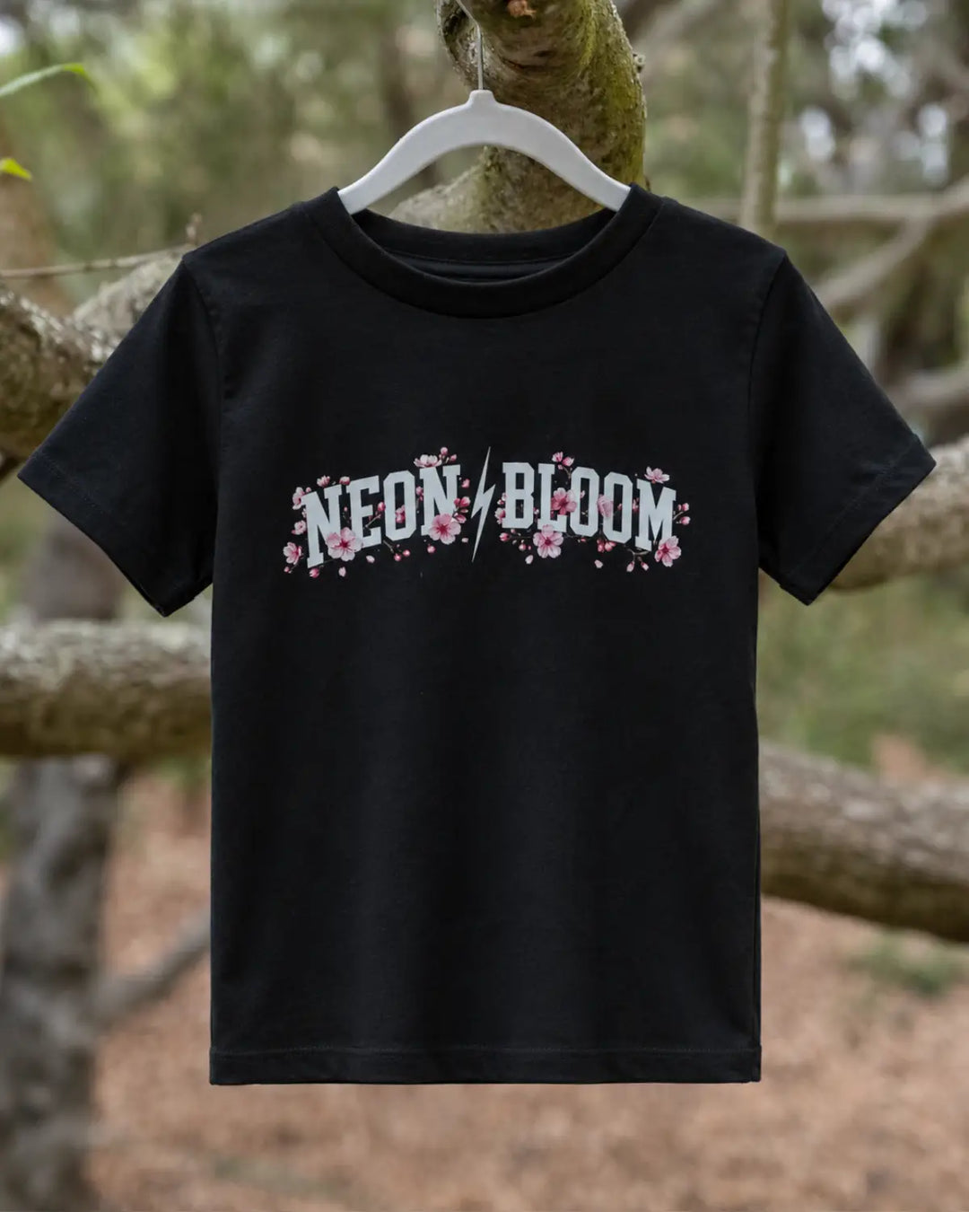 Black t-shirt with 'NEON BLOOM' text with cherry blossoms on a hanger against a natural background