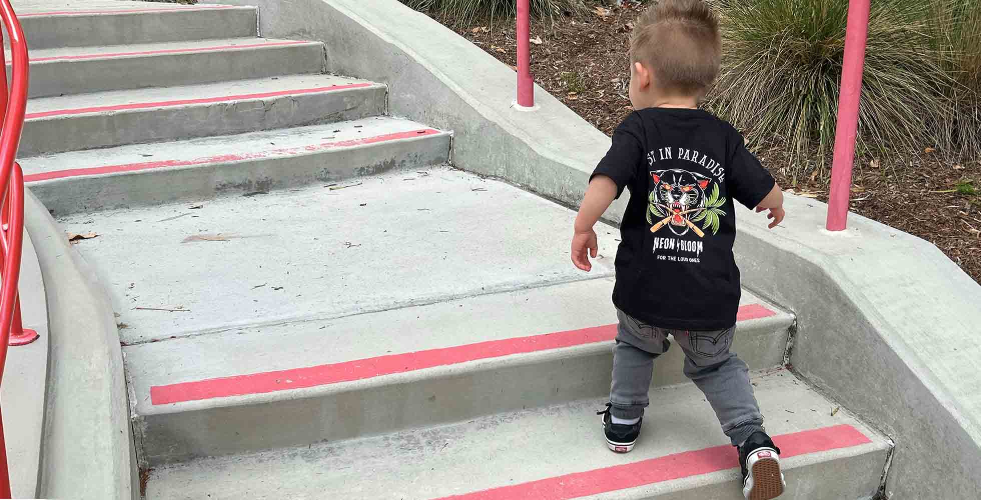 Child in a black t-shirt walking up a set of concrete stairs with pink railings.