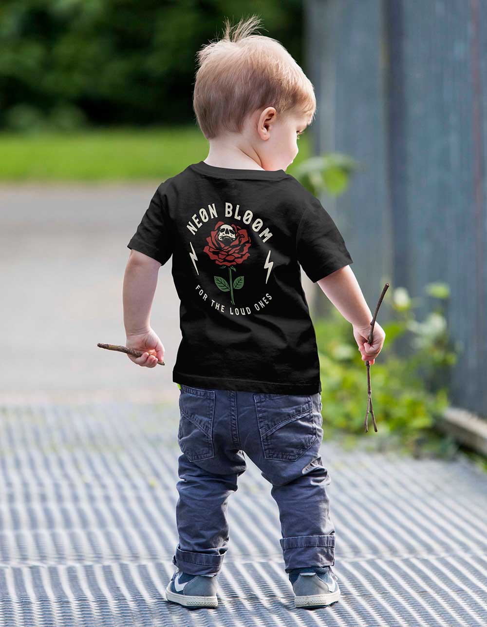 Child wearing a black t-shirt with 'Keen Bloom' design outdoors.